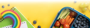 A notebook, raw vegetables and blueberries sit on a yellow background.