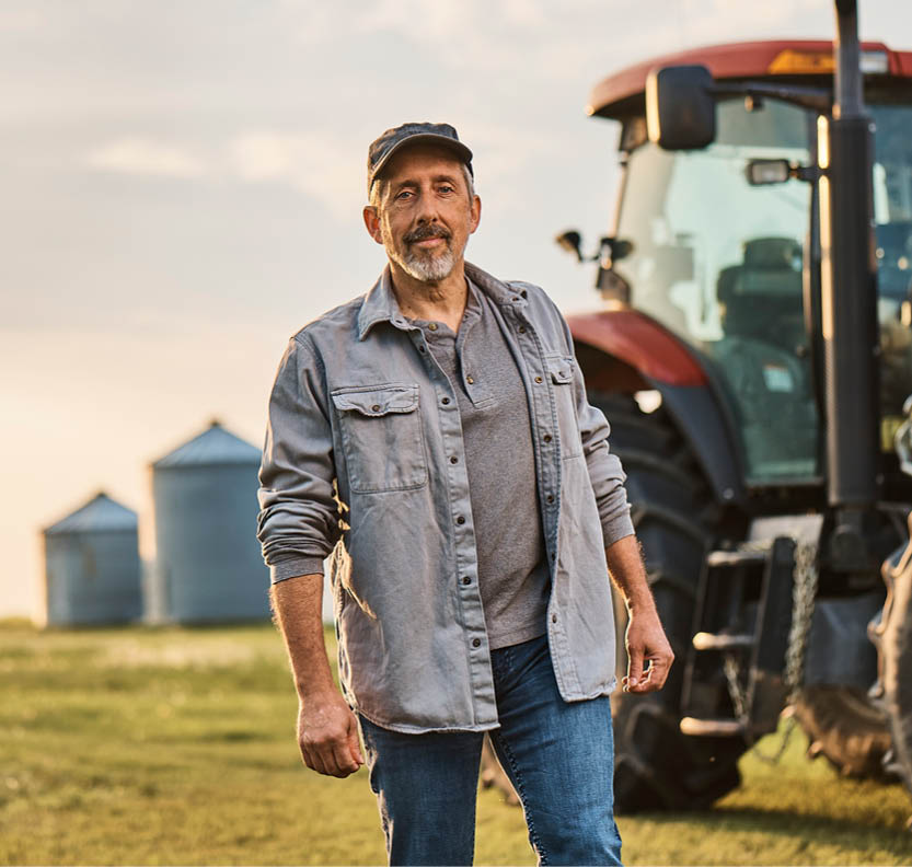 A famer stands in a filed next to a tractor.