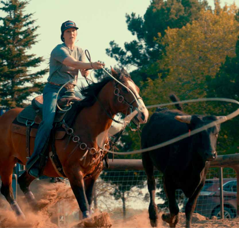 A female riding a horse ropes a calf.