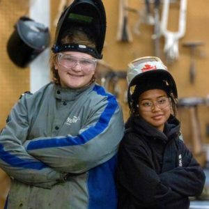 Two female students wear protective masks and jackets for welding.
