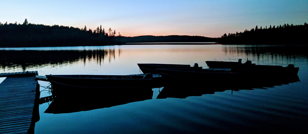 Docked boats rest on the glassy water of a lake at sunset