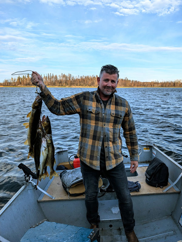 Matt Brown holds up his fishing catch while standing in a boat on Mirond Lake.